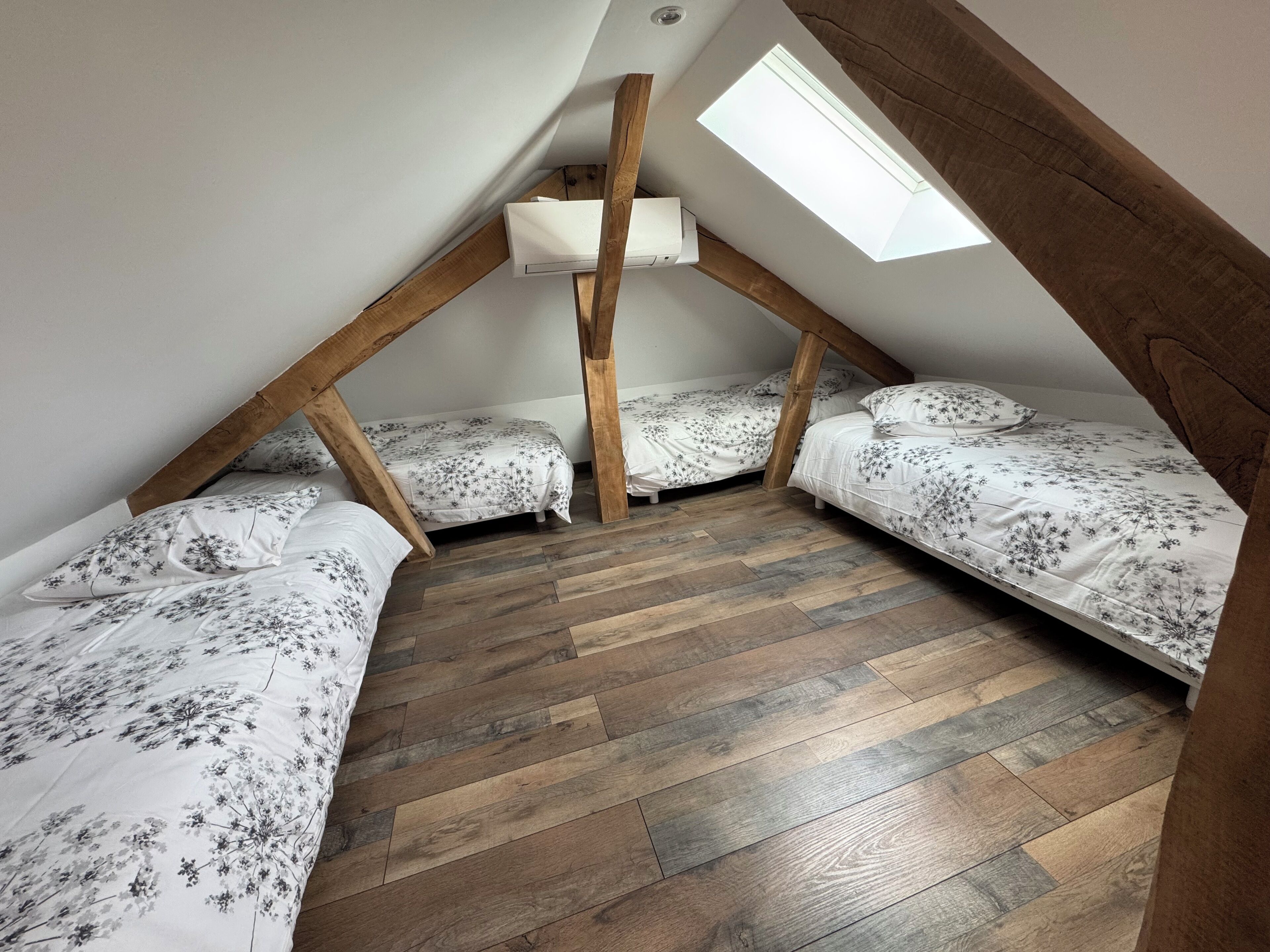 Un dormitorio estilo ático con tres camas, vigas de madera y un tragaluz.