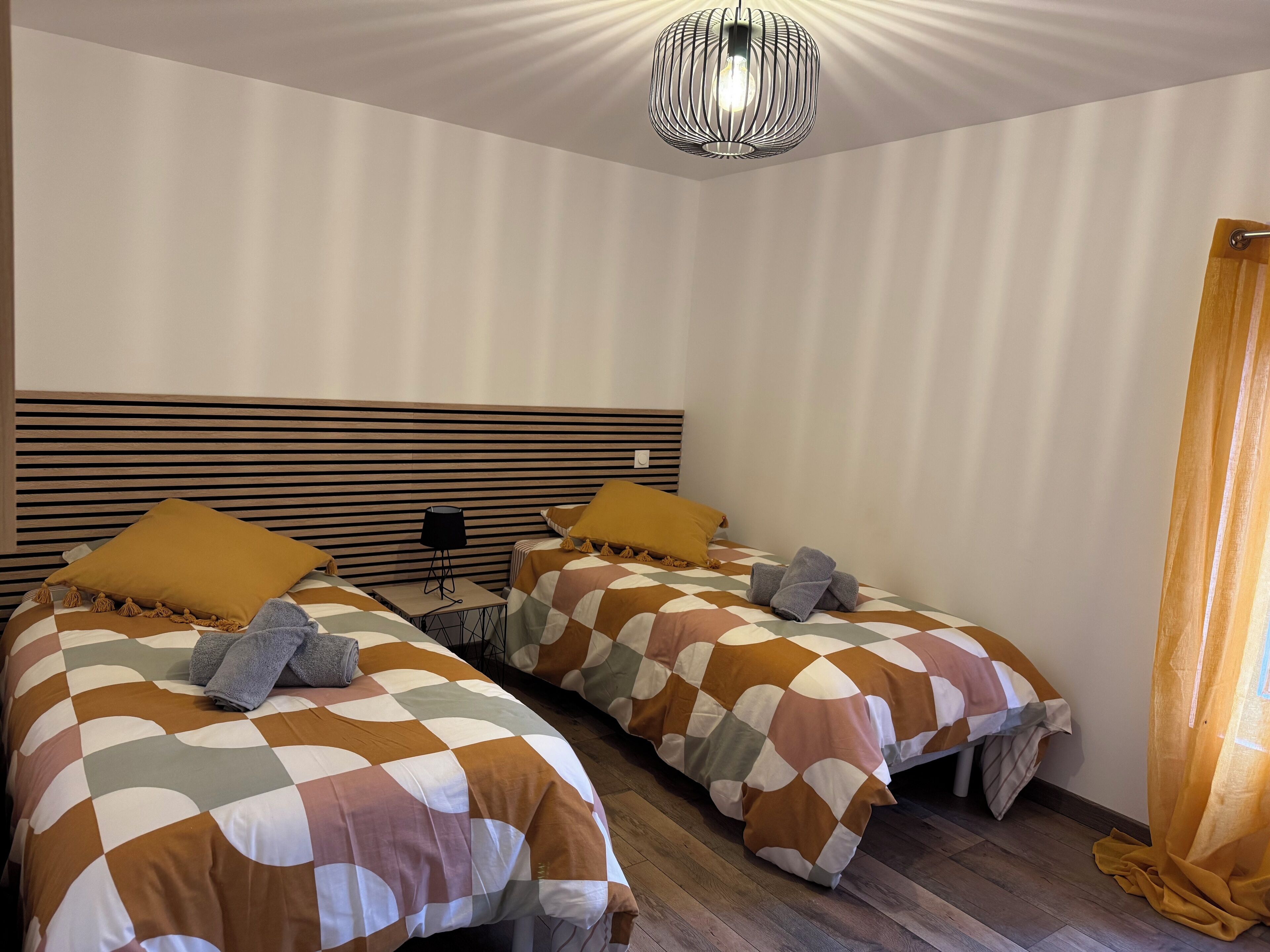 Une chambre d’hôtel avec deux lits, chacun recouvert d’une couvre-lit à carreaux, doté d’une tête de lit en bois et agrémenté d’une lampe noire posée sur une table de chevet.