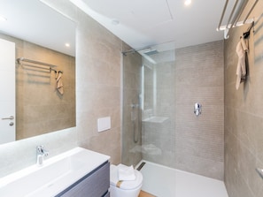Ein modernes Badezimmer mit einer begehbaren Glasdusche, einem weißen Waschbecken und einem großen Spiegel.