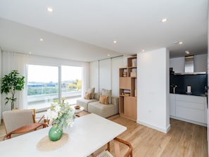 Ein modernes Apartment mit Essbereich, Sofa, Küche und großen Fenstern mit Blick auf die Stadt.