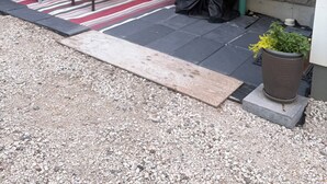 Een terras met een rood-wit gestreepte vloerkleed, een zwarte barbecue en een potplant.