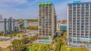 A hotel with multiple floors, a swimming pool, and a landscaped area with palm trees. - One bedroom ocean view Meridian plaza (Myrtle Beach)