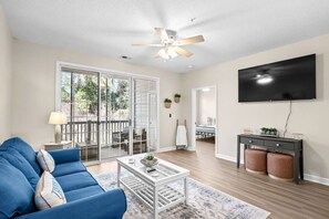 Ein Wohnzimmer mit einem blauen Sofa, einem Couchtisch, einem Fernseher und einer Schiebetür zu einer Außenpatio.