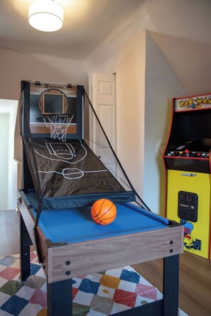 En liten basketplan inomhus med en korg, en basketboll och en Pac-Man-spelautomat.