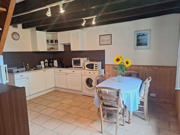 Cocina compacta con armarios blancos, lavadora y comedor con mesa y sillas.