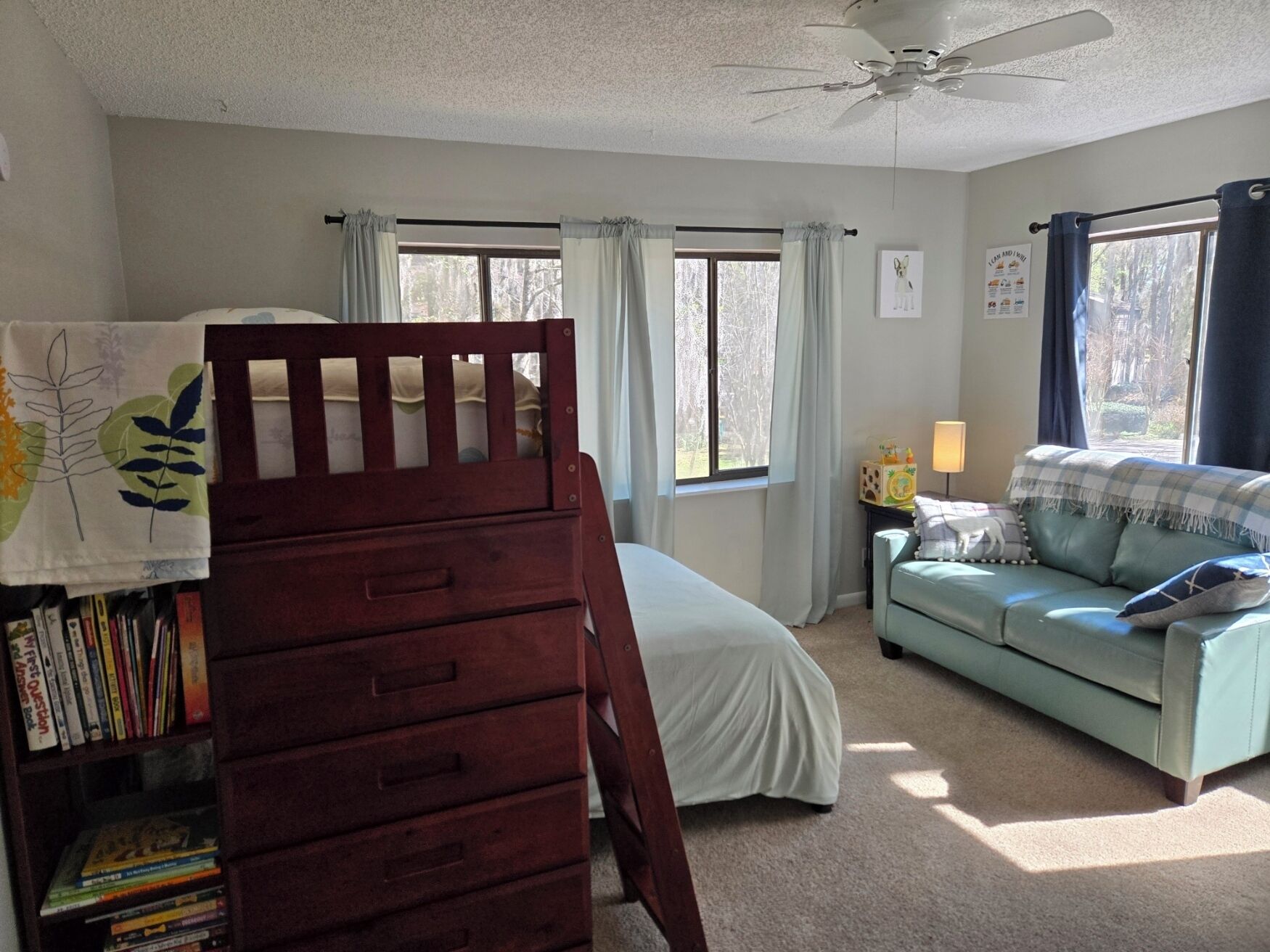 Un dormitorio con una cama, un aparador de madera, una estantería, un sofá verde y una ventana con cortinas.