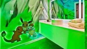 A bathroom with a green-themed wall mural, a sink with a mirror, and a towel rack. - Pokemon studio w/ Disney shuttle & pool (Kissimmee)