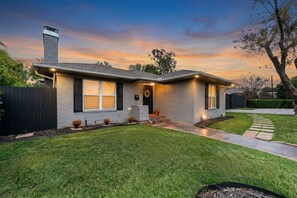 A two-story house with a brick exterior, a front porch, and a well-maintained lawn. - Mockingbird Nest - 4BR Sleeps 8. Fenced Yard. Fire Pit. Gated Parking (Dallas)