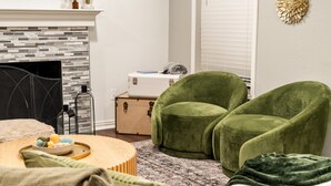 A cozy room with a fireplace, green armchairs, a wooden coffee table, and a patterned rug. - Spacious 4BR Home - King Suite - Family Friendly - Near Dallas Attractions (Dallas)