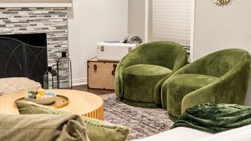 Een knus vertrek met een open haard, groene fauteuils, een houten salontafel en een vloerkleed met dessin.