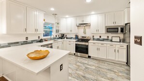 A modern kitchen with white cabinets, a large island, and a stainless steel refrigerator. - Spacious 4BR Home - King Suite - Family Friendly - Near Dallas Attractions (Dallas)