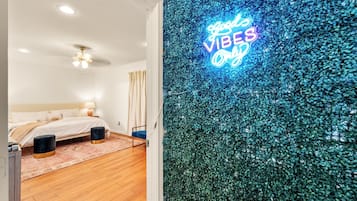 Een slaapkamer met een bed, nachtkastjes, een plafondventilator en een neonbord aan de muur.