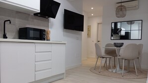 Una cocina moderna con armarios blancos, un microondas negro y una zona de comedor con dos sillas y una pequeña mesa.