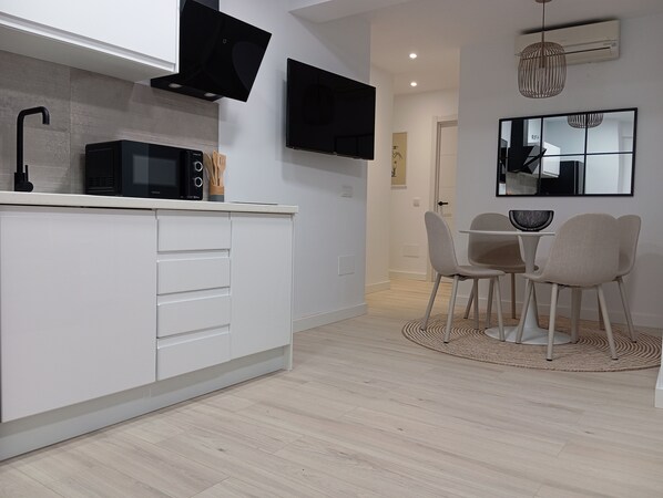 Een moderne keuken met witte kasten, een zwarte magnetron en een eethoek met twee stoelen en een kleine tafel.