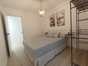 Een slaapkamer met een bed, een hanglamp, een nachtkastje en twee aan de muur bevestigde schilderijen.