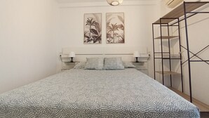 Un dormitorio con una cama, dos lámparas de pared, una lámpara colgante y dos impresiones enmarcadas de motivos botánicos.