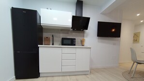 Una cocina moderna con un refrigerador negro, gabinetes blancos, un microondas y un televisor de pantalla plana montado en la pared.
