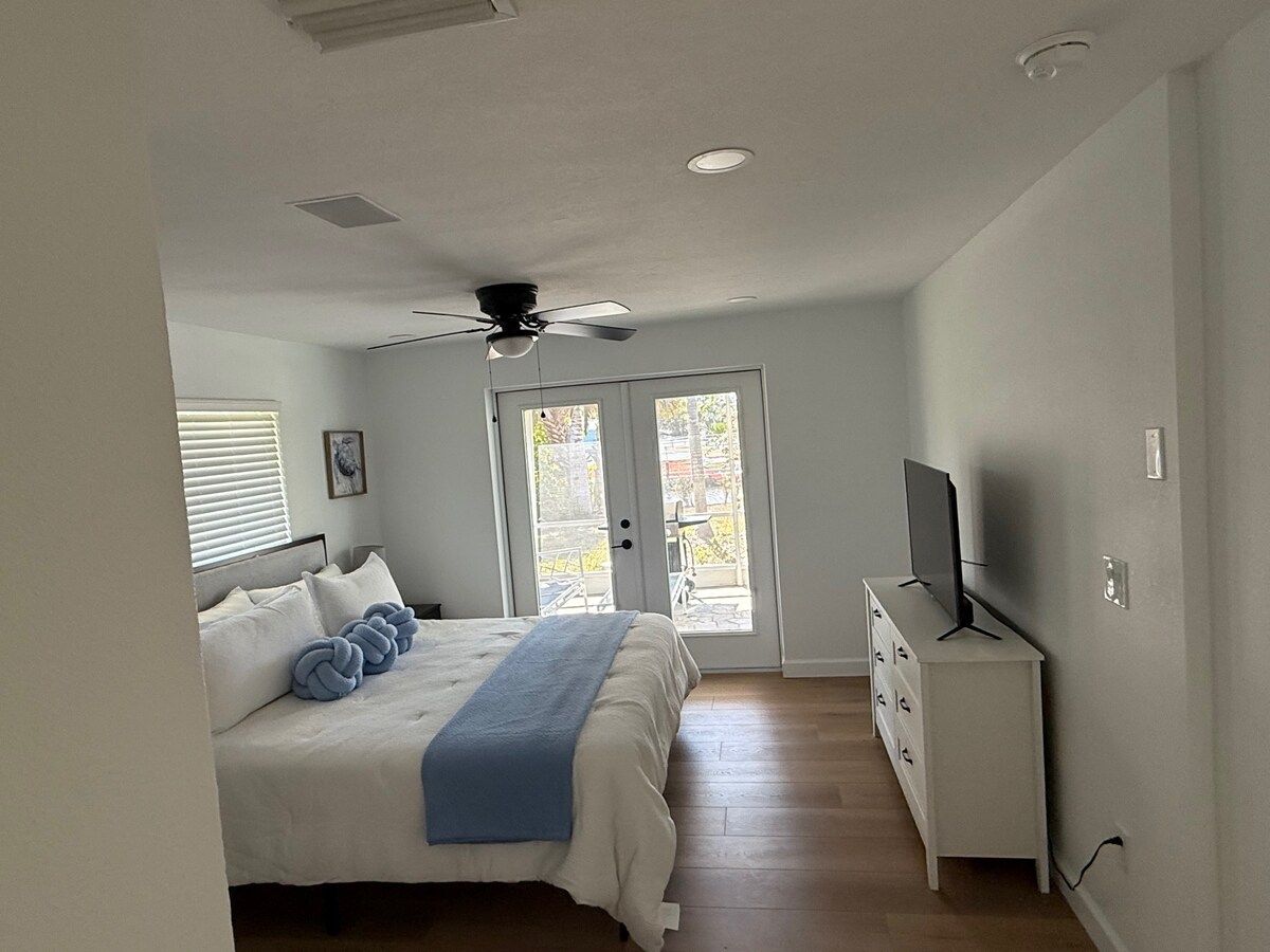 A bedroom with a bed, a television on a dresser, and a ceiling fan.