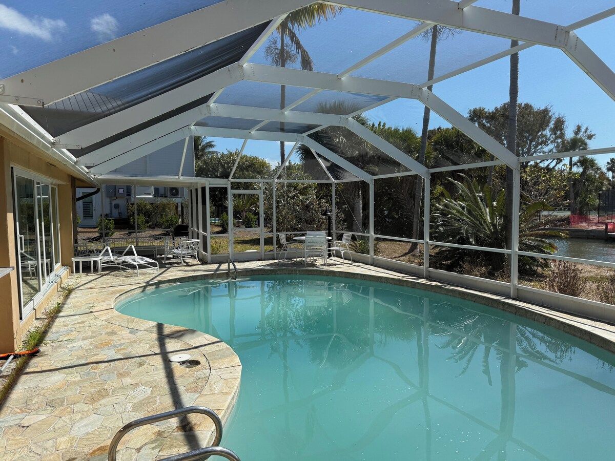 A swimming pool with a covered area, stone flooring, and outdoor furniture.