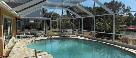 A swimming pool with a covered area, stone flooring, and outdoor furniture.