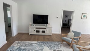 Ein Wohnzimmer mit einer weißen Unterhaltungseinheit, einem Flachbildfernseher, einem gemusterten Teppich und einem blauen Sessel.