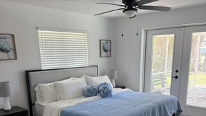 Ein Schlafzimmer mit einem Bett, einem Nachttisch, einem Deckenventilator und einer Tür, die auf einen Balkon führt.