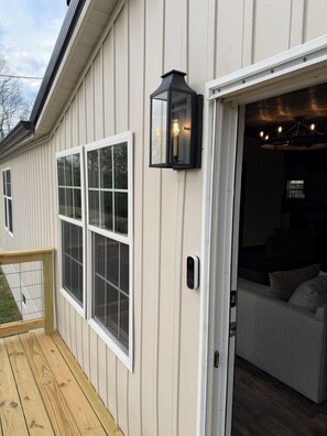 A house with a deck, a sliding glass door, and a black exterior light fixture. - NEW! Spacious Farmhouse Cabin, 30 acres w/ Firepit, Pond, Waterfall, Trails (Zoe)