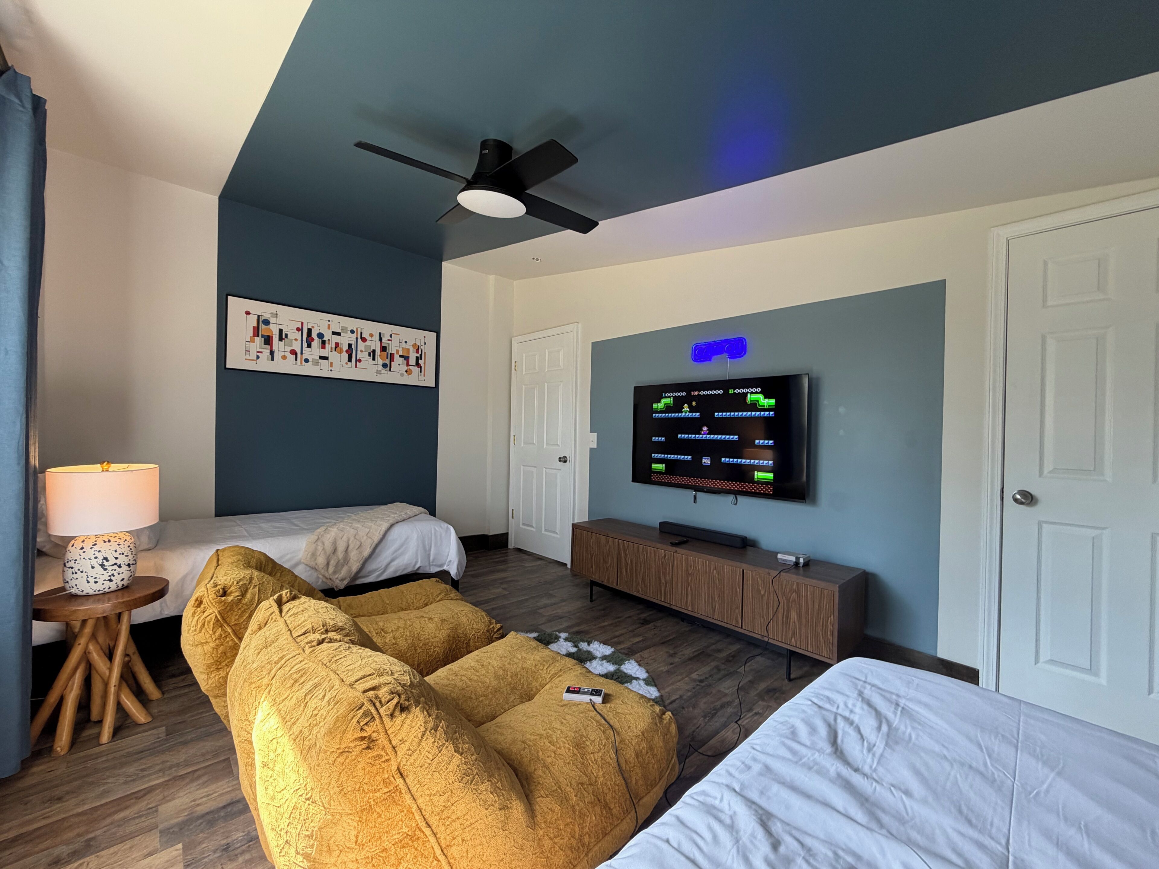 Une chambre d’hôtel avec deux lits, un ventilateur de plafond, une télévision, une lampe et un tableau au mur.