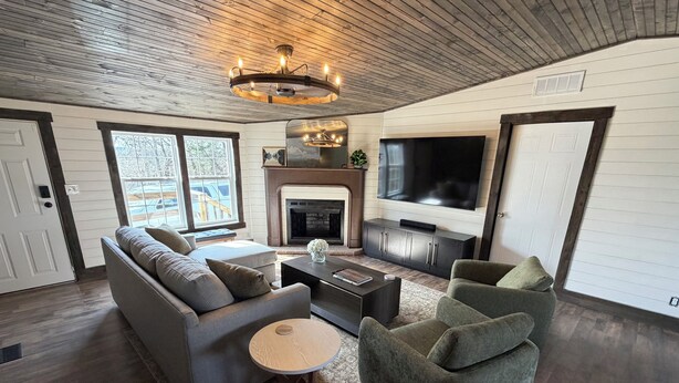 A living room with a sofa, armchairs, a coffee table, a fireplace, a TV, and a wooden ceiling. - NEW! Spacious Farmhouse Cabin, 30 acres w/ Firepit, Pond, Waterfall, Trails (Zoe)