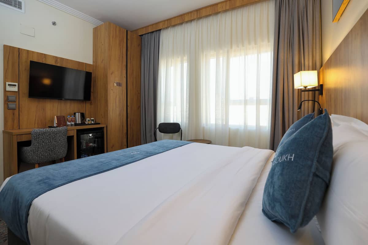 Une chambre d’hôtel équipée d’un lit, d’un bureau, d’une chaise, d’une télévision et d’une fenêtre avec des rideaux.