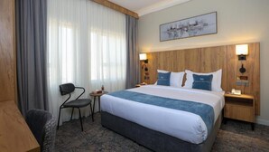 Ein Hotelzimmer mit einem großen Bett, einem Holzkopfteil, einem kleinen Schreibtisch, einem Stuhl und einem Vorhangfenster.