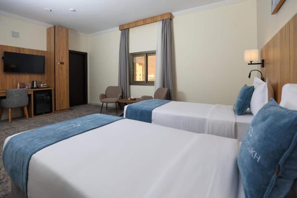 Une chambre d’hôtel avec deux lits, un bureau, une chaise, une télévision et une fenêtre avec des rideaux.