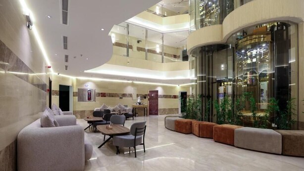 Eine großzügige Lobby mit hoher Decke, mehreren Sitzbereichen und einer zentralen Treppe.