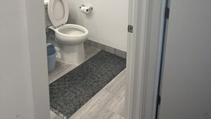 Ein Badezimmer mit Toilette, einem blauen Mülleimer und einer weißen Tür.