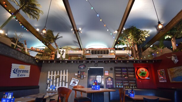 A restaurant with booths and tables, string lights, and a neon sign.