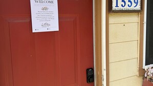 A red door with a welcome sign, a keypad lock, and a house number sign.
