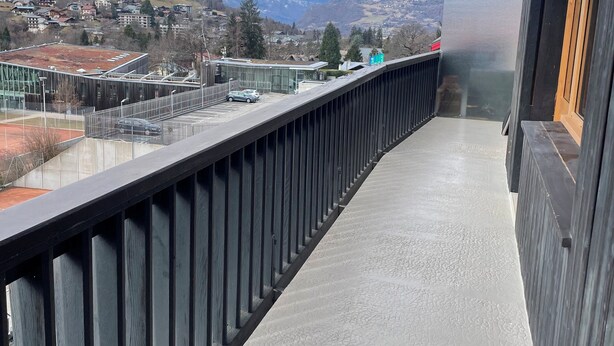 A balcony with a view of snow-capped mountains, a modern building with a glass facade, and a paved walkway. - Mountain apartment 5 minutes from the center of Saint Gervais les Bains (Saint-Gervais-les-Bains)