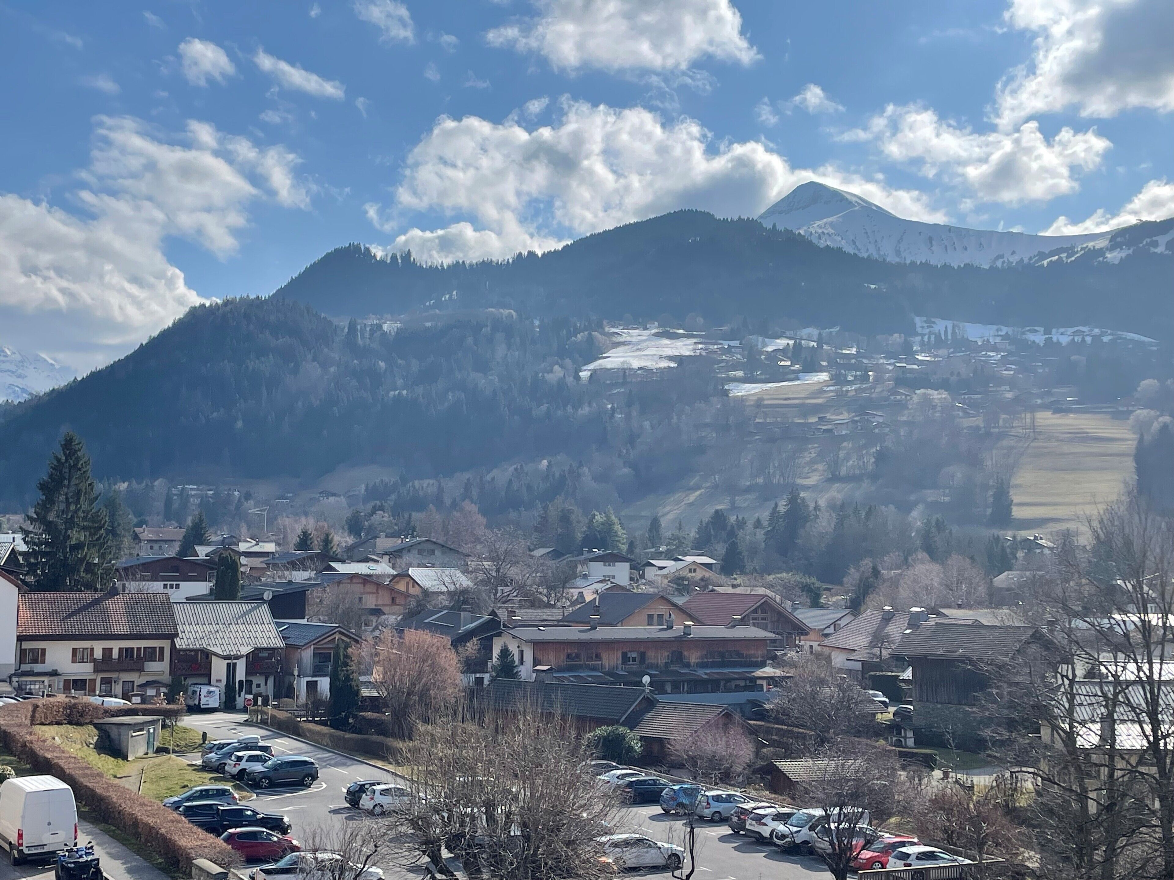 Une ville située au pied d’une montagne, avec des immeubles résidentiels, un parking et un ciel dégagé.