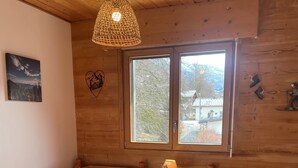 A wooden cabin room with two beds, a window, a hanging light, and a small table. - Mountain apartment 5 minutes from the center of Saint Gervais les Bains (Saint-Gervais-les-Bains)