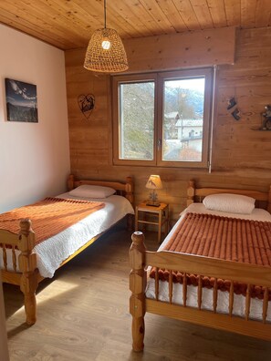 Habitación de cabaña de madera con dos camas, una ventana, una lámpara colgante y una pequeña mesa.