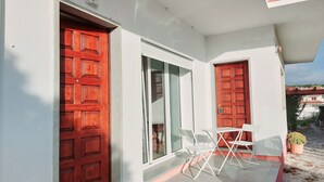 A building with two red doors, a glass door, and a small outdoor seating area with white chairs. - Family apartment in a quiet area 5 minutes from the beach! (Nazaré)