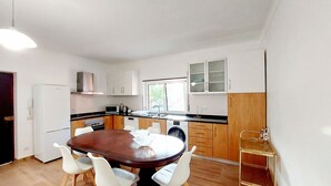 A compact kitchen with white cabinets, a dining table with chairs, and a small window. - Family apartment in a quiet area 5 minutes from the beach! (Nazaré)
