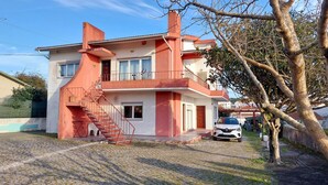 A two-story house with a red and white exterior, a visible staircase, and a parked car in the driveway. - Family apartment in a quiet area 5 minutes from the beach! (Nazaré)