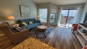 Un salon avec un canapé bleu, un fauteuil marron, une table basse en bois et un tapis à motifs.
