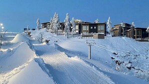 A snow-covered ski slope with modern buildings and trees.