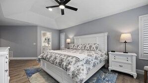Une chambre à coucher comprenant un lit, des tables de chevet, une commode, un ventilateur de plafond et un grand miroir.