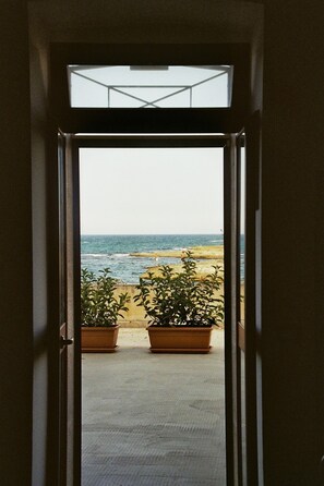 A doorway leading to a beach view with two potted plants on the floor. - Seafront apartment with terrace, veranda & interesting extras (Villanova)