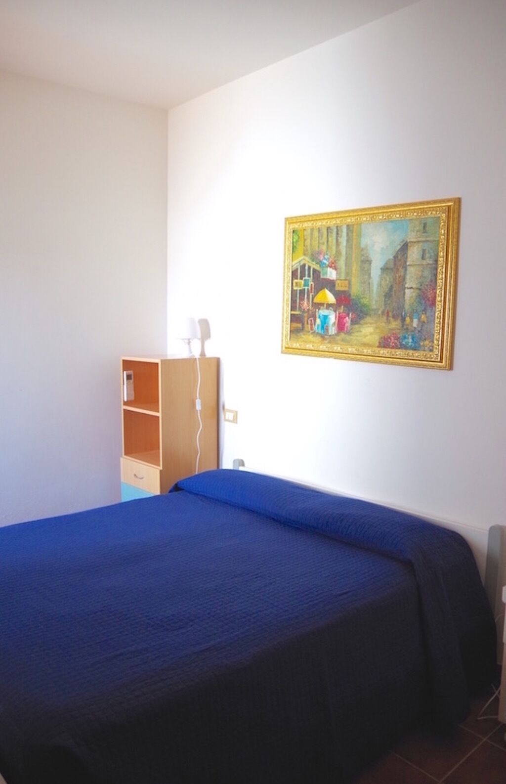 Una habitación con una cama, un armario de madera y un cuadro en la pared.