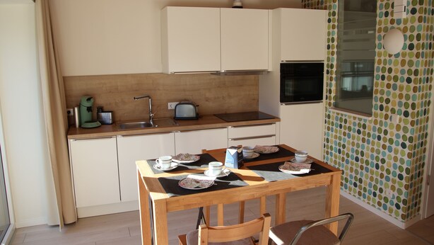 Uma cozinha compacta com uma mesa de jantar posta para dois, uma janela com vista e uma parede com padrão de bolinhas.