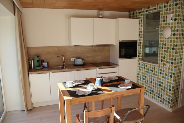 A compact kitchen with a dining table set for two, a window with a view, and a polka dot wall.